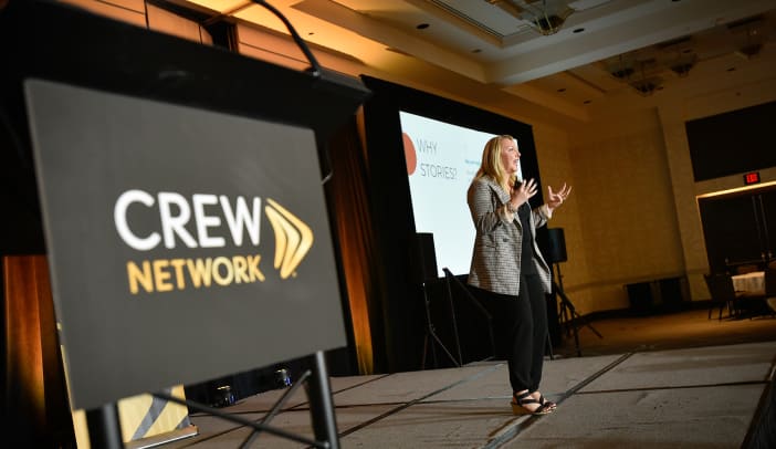 Woman speaking from stage in front of CREW network sign