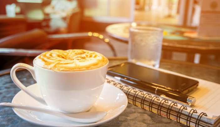 coffee cup on table with notebook, pen, smartphone, cafe