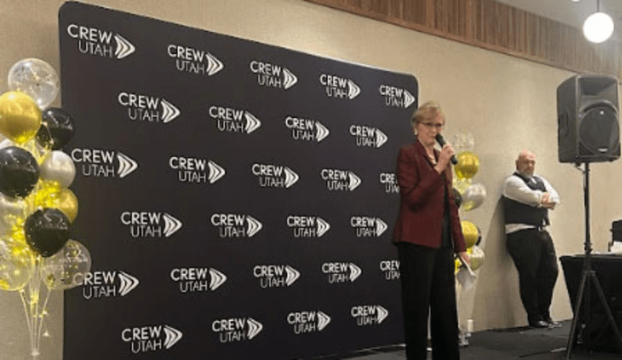 Gwen Knight speaking on stage in front of CREW Utah banner.