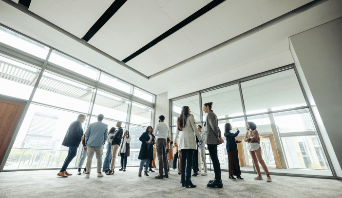 Businesspeople attending a corporate event, networking and engaging in discussions in a large, modern, bright office space.