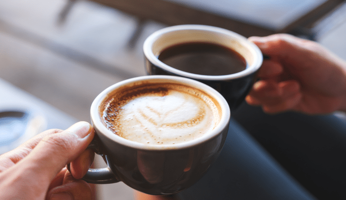 two specialty coffee drinks in mugs in hands in toast mode