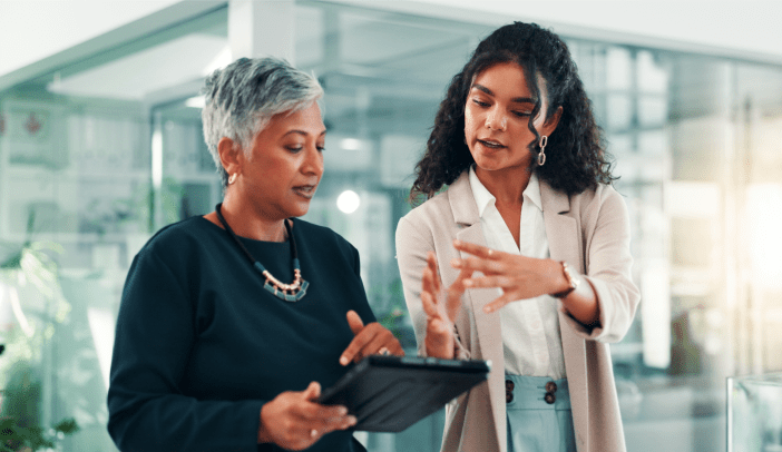 Two women looking at a tablet together; one is younger, suggesting a mentoring relationship.