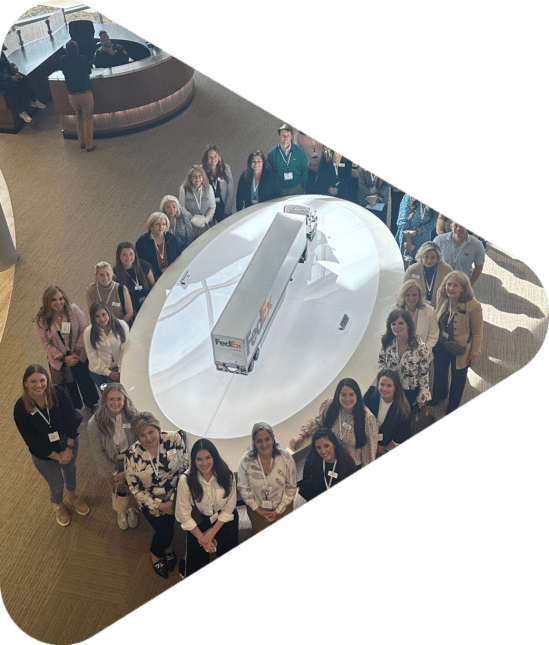 Women standing in an oval around a table with a model semi on it