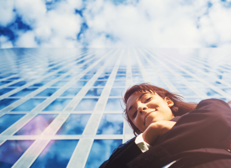 businesswoman looking down at camera in front of glass skyscraper