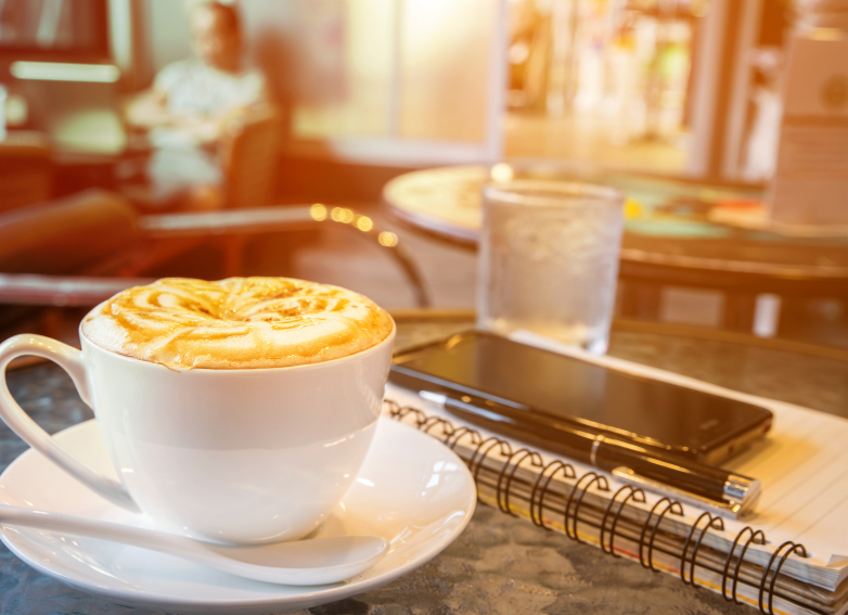 coffee cup on table with notebook, pen, smartphone, cafe