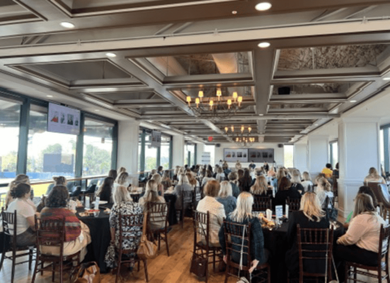 Room full of guests at round tables watching panel