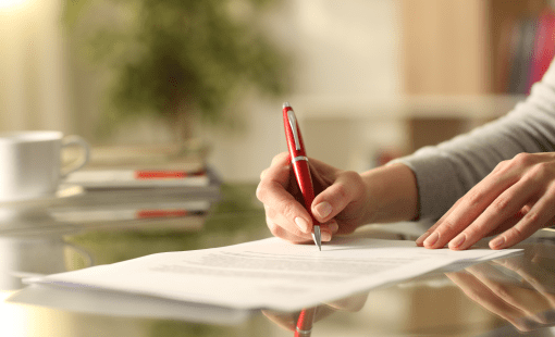 Close up of woman hands signing document with pen on a desk at home