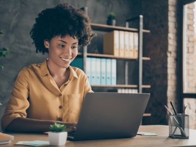 Photo of cheerful positive, mixed-race girl smiling toothily working on laptop