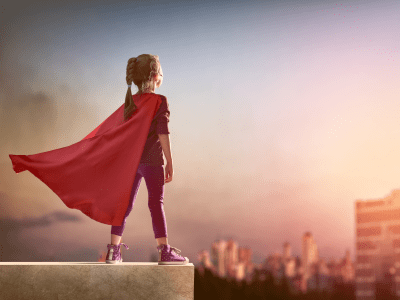 little girl in a red cape looking on a city skyline