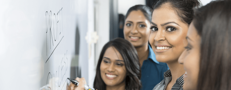 Indian business woman writing on a whiteboard with her team around her.