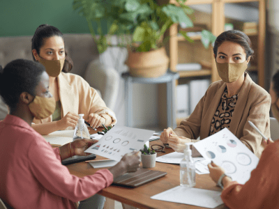 High angle view at multi-ethnic group of young businesswomen wearing masks during meeting in office, copy space