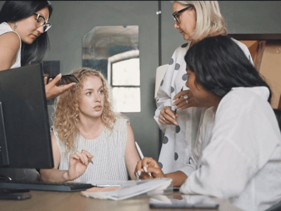 four women working around computer in office