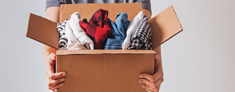 Unrecognizable woman holding box with clothes in it. close-up. Clothing donation.