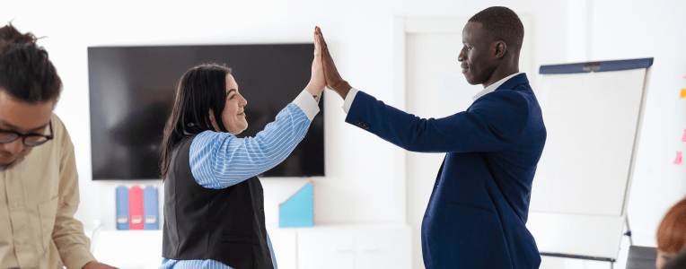 Caucasian woman and African man colleagues high five during a meeting in boardroom. Celebration of success, cooperation and inclusivity concept.