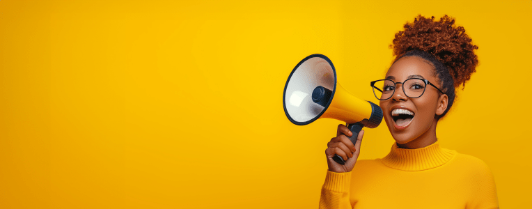 Happy young Black woman in yellow sweater, announcing sale offers through a megaphone, isolated on a yellow background with copy space. Screaming into the megaphone. Studio portrait.