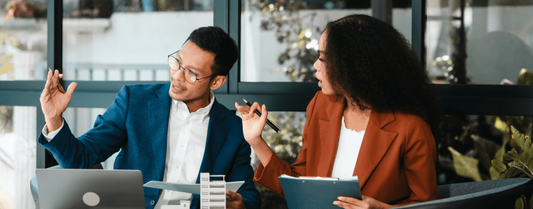 Attractive Asian businessman and African American female real estate and land investor talk discussing together on table with laptop and small building model. Reserve fund.