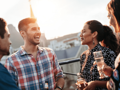 Happy young man chatting and laughing with friends. Young people having a good time together during rooftop party.