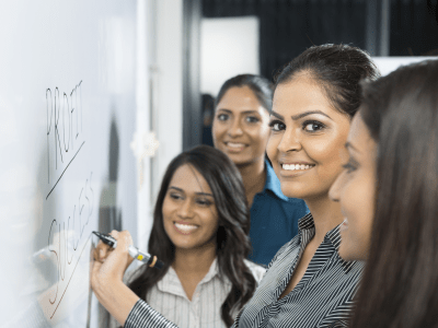 Indian business woman writing on a whiteboard with her team around her.