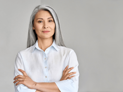 Stylish confident adult 50 years old Asian female psychologist standing arms crossed looking at camera at gray background. Portrait of sophisticated grey hair woman advertising products and services.