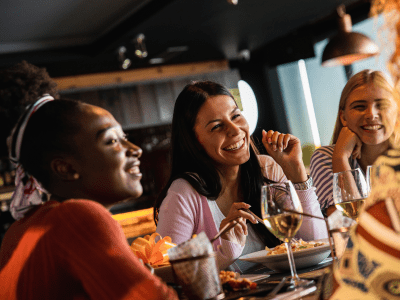 Group of young female friends having fun in restaurant, talking and laughing while dining at table.