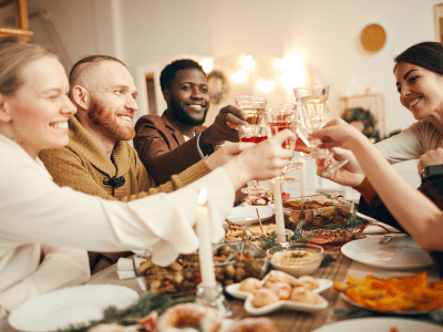 Multi-ethnic group of people raising glasses sitting at beautiful dinner table celebrating Christmas with friends and family, copy space