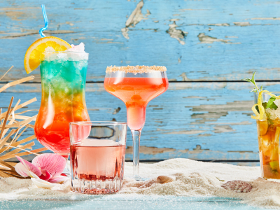 Exotic summer drinks on white beach sand, viewed from the front against blue wooden background