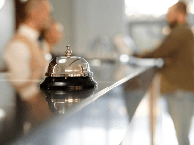 Modern luxury Hotel Reception Counter desk with Bell. Service Bell locating at reception. Silver Call Bell on table, Receptionists and customer on background. Сheck in hotel. Concept.
