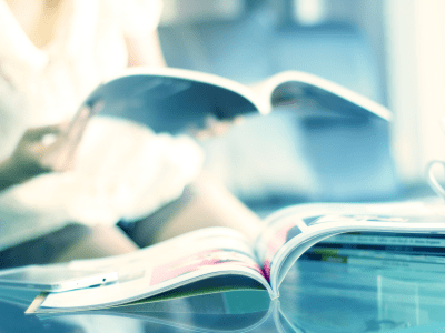 magazine open on table with woman reading magazine in the background