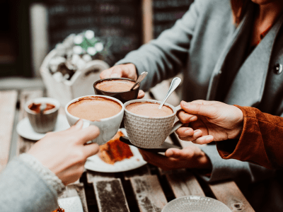 Group of young friends drinking coffee with cakes in an outdoor cafe in Porto, Portugal. Holding their cups together. Close up. Lifestyle.