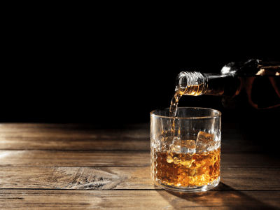 Pouring whisky into glass on wooden table closeup