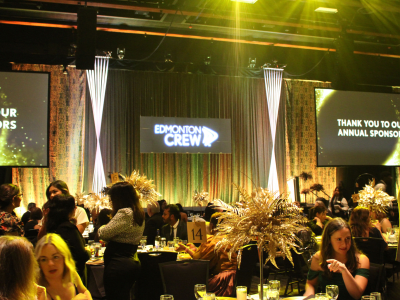 People sitting around tables with screens and stage in background.