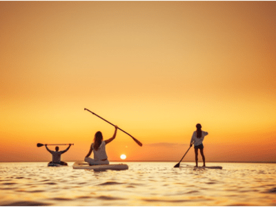 Three people paddle boarding at sunset