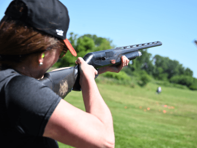 woman in baseball hat holding a gun and shooting at clay