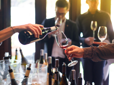 someone pouring a taste of red wine, others in background tasting