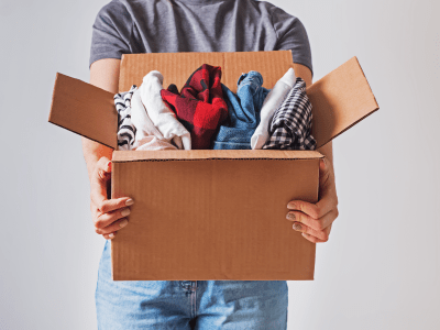 Unrecognizable woman holding box with clothes in it. close-up. Clothing donation.