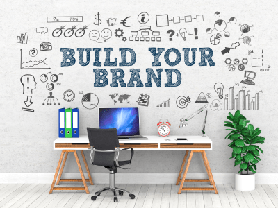 Build Your Brand written on wall above desk with laptop.