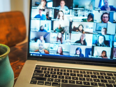 Close up of coffee mug and laptop on a virtual meeting with a grid of diverse faces.