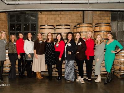 Group of women standing in front of whisky barrells at a holiday party.