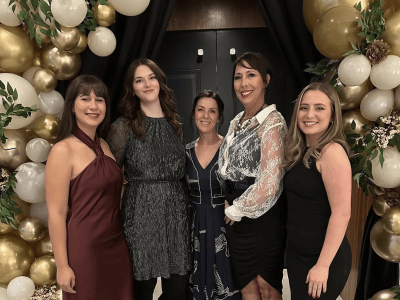 group of 5 women at 2025 Gala event, standing by a balloon arch of white and gold balloons