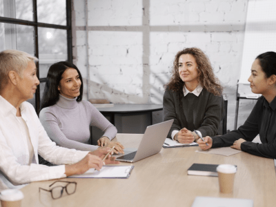 Four diverse women colleagues working together at a table with a laptop.