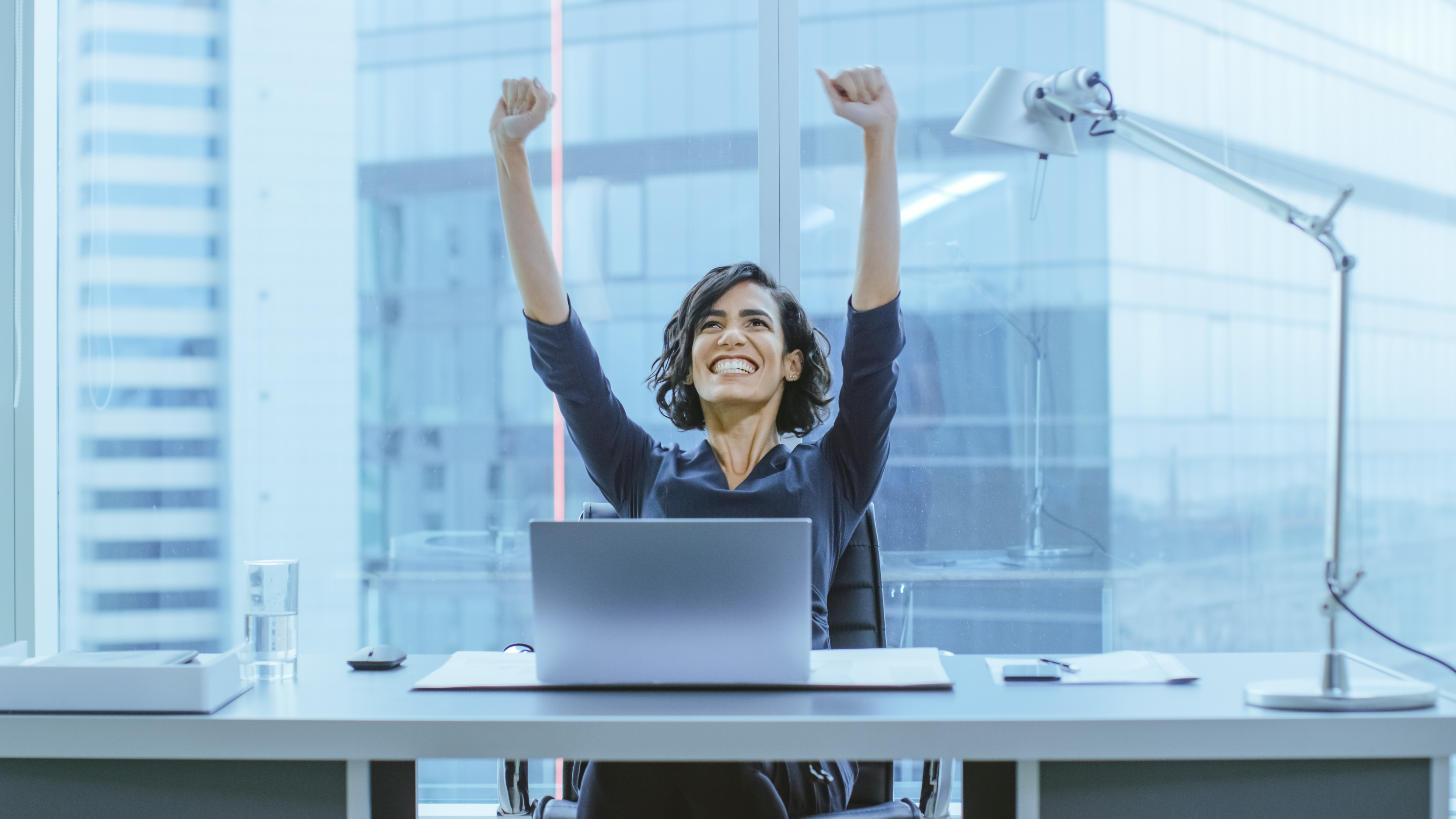 Shot of the Beautiful Businesswoman Sitting at Her Office Desk, Raising Her Arms in a Celebration of a Successful Job Promotion.