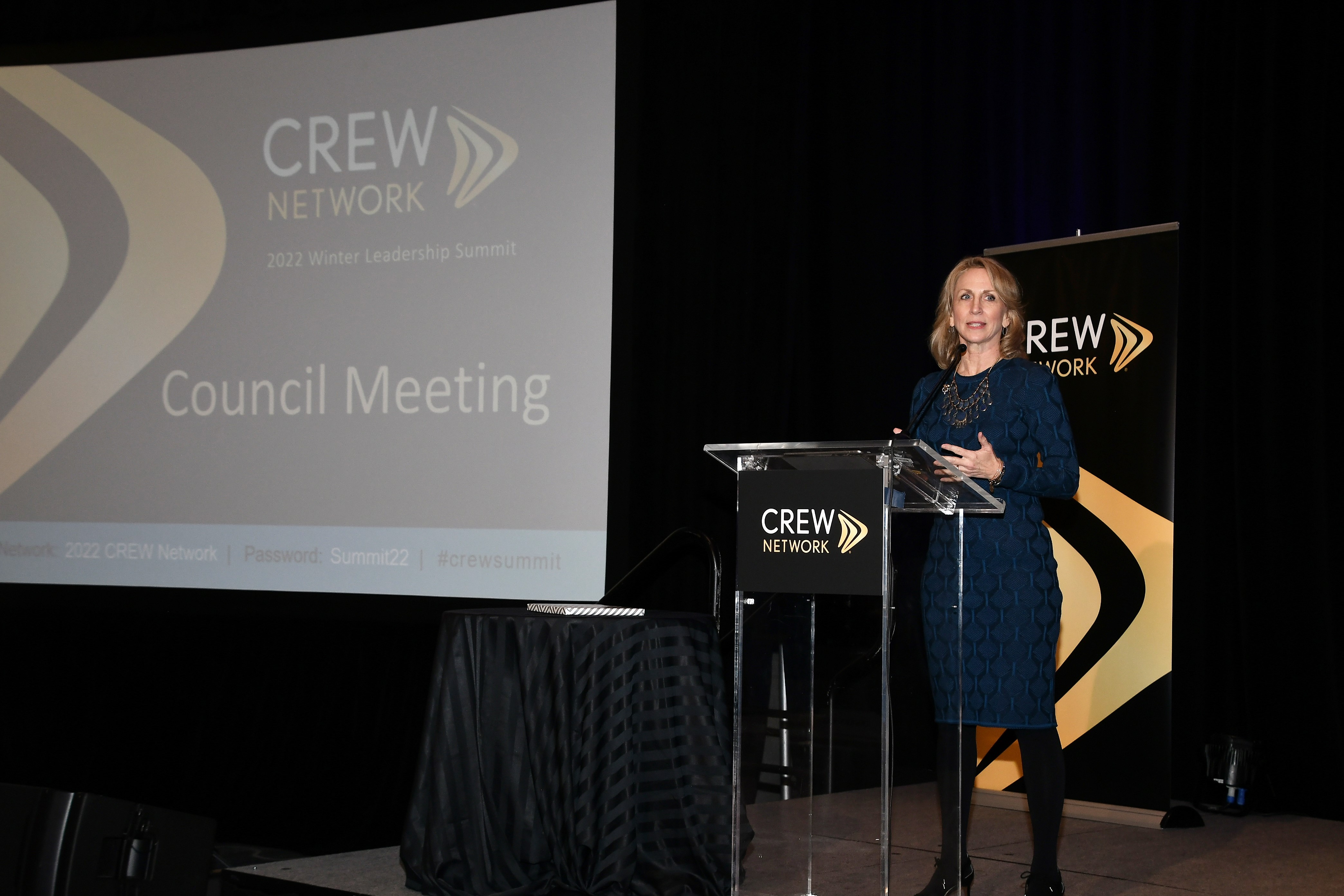 Woman speaking at a glass podium at a CREW Network summit