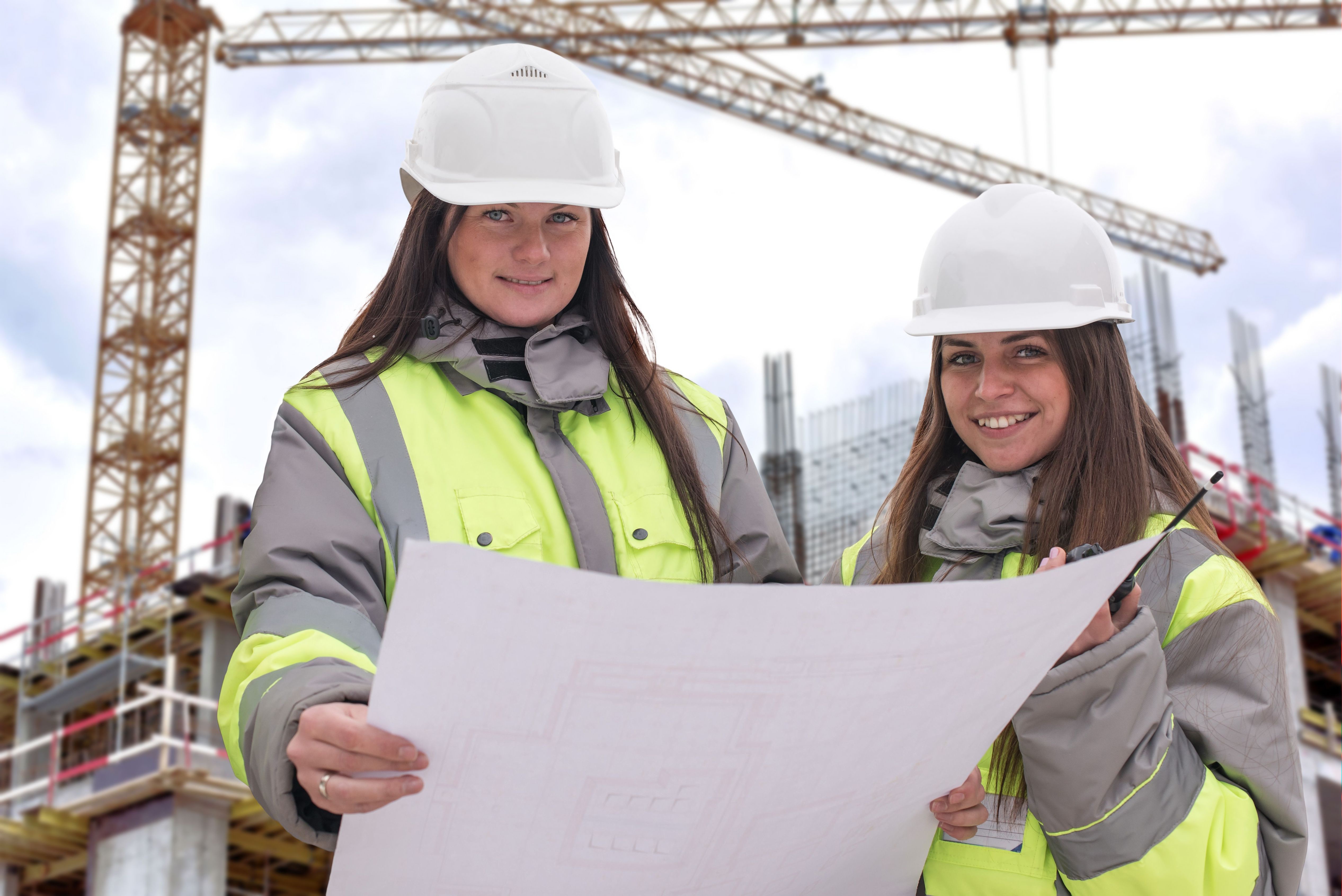 young female students smiling in hard hats looking at blueprints