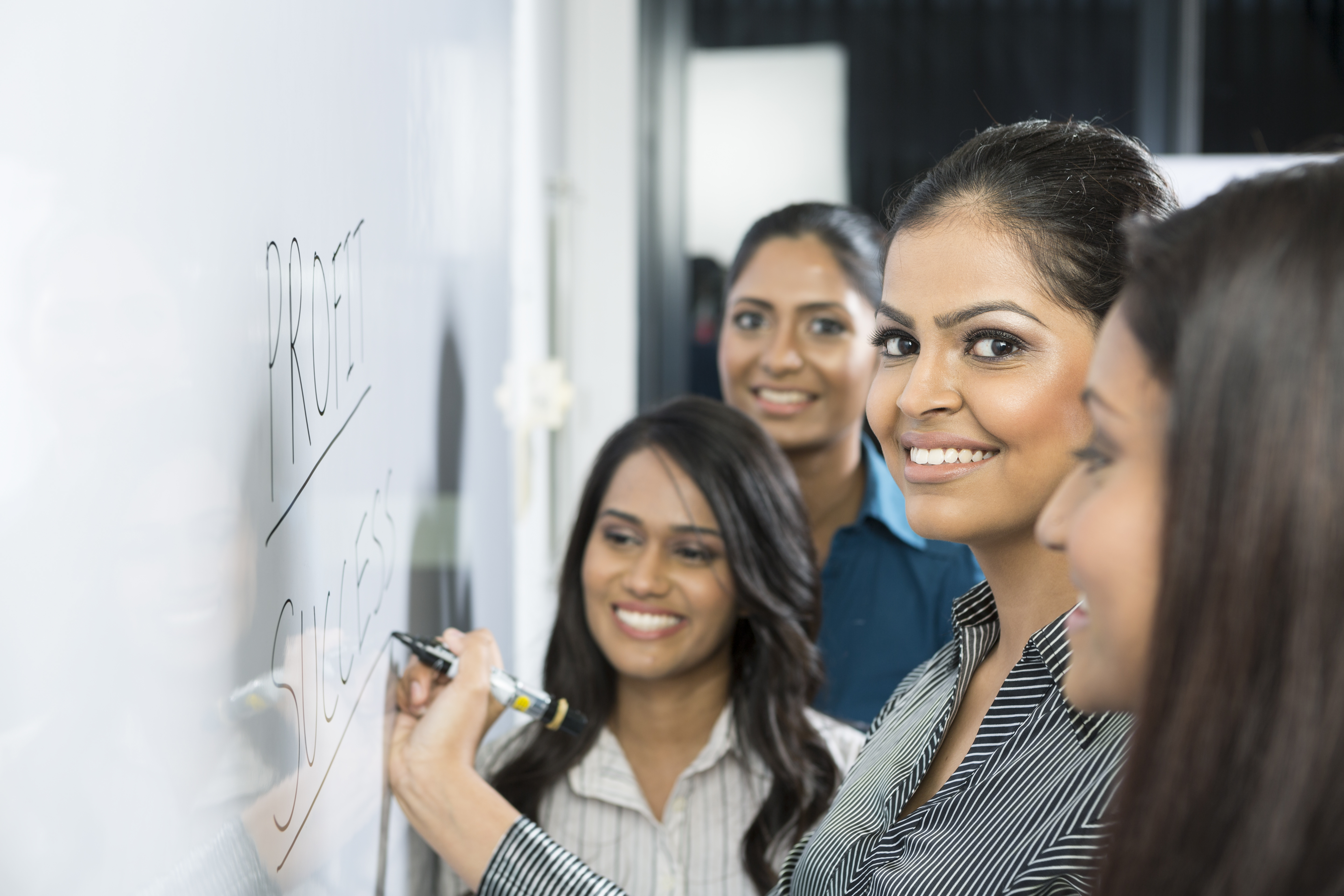 Indian business woman writing on a whiteboard with her team around her.