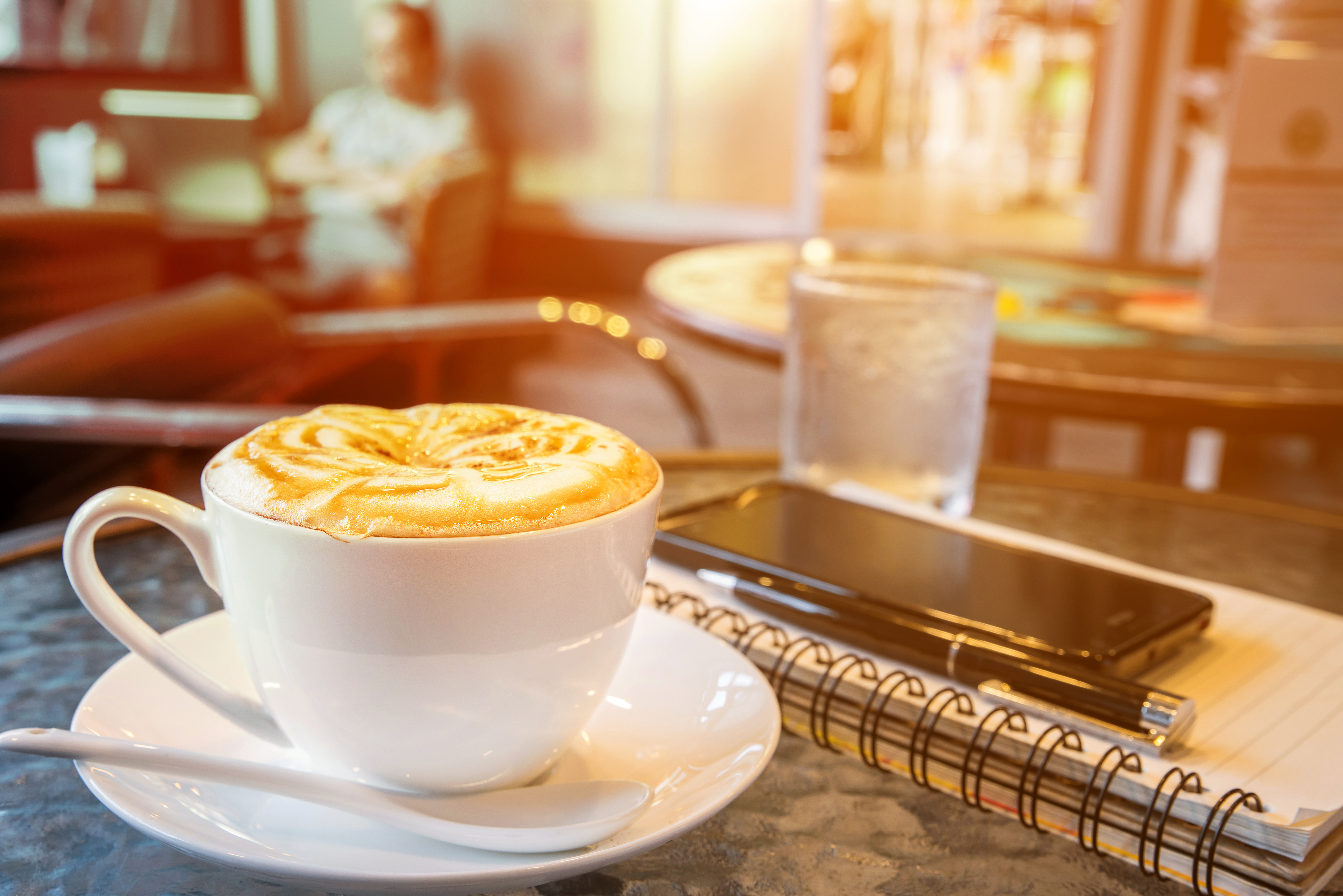 coffee cup on table with notebook, pen, smartphone, cafe