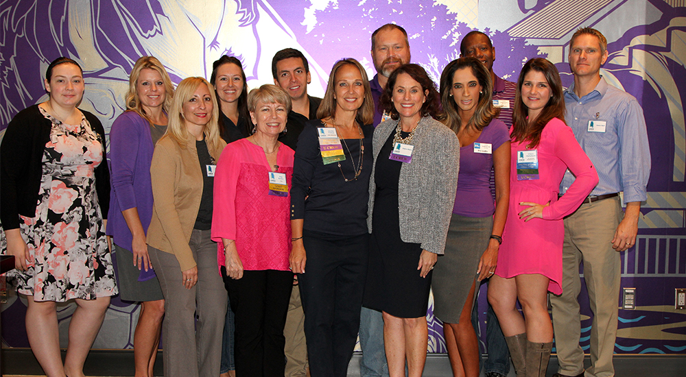 group of event attendees posing against purple and white background mural