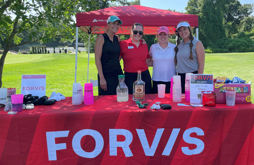 four women posing behind FORVIS stand on green at golf event